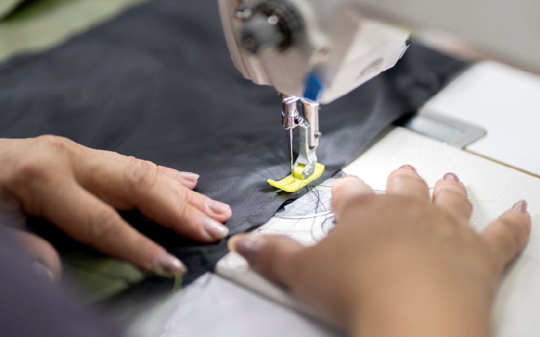 Handen die textiel onder een naaimachine doorvoeren